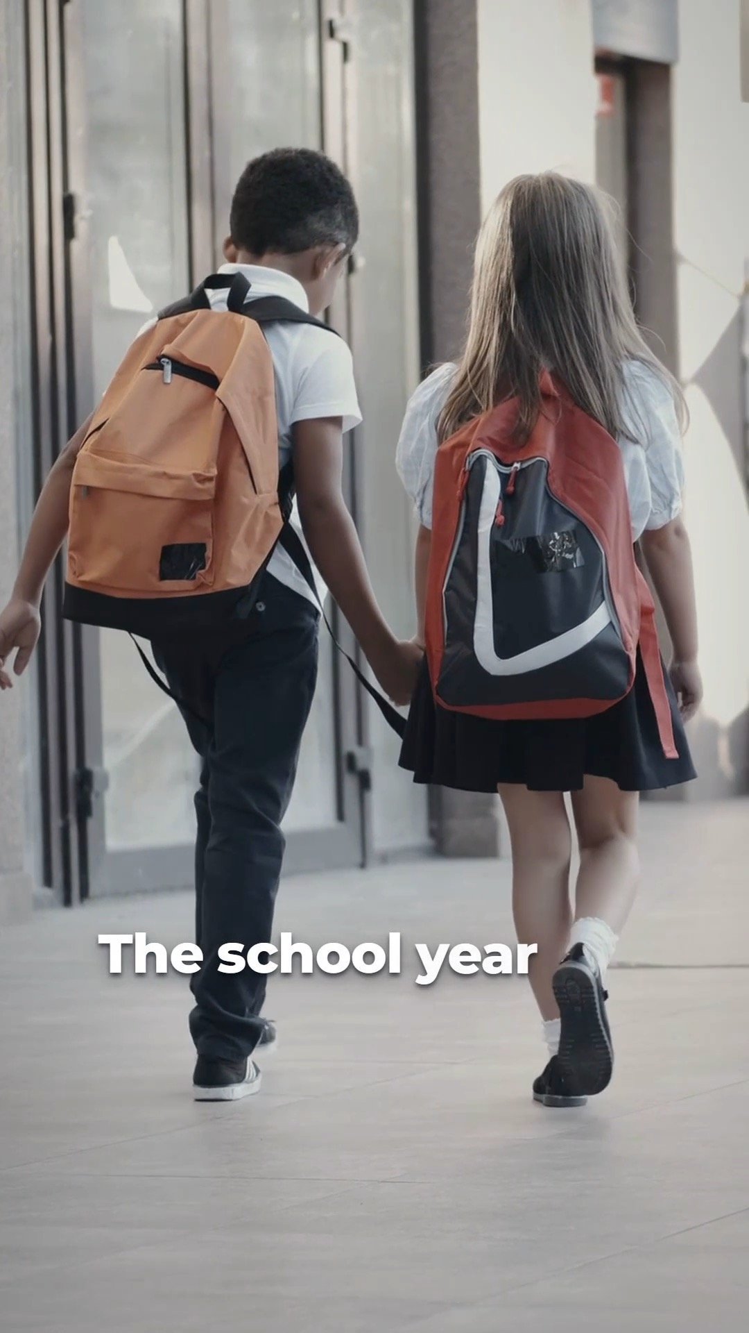 Two students with backpacks walking hand in hand down a school hallway